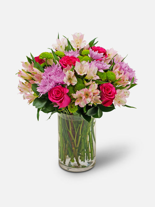 marvel bouquet with pink roses, pom poms, and alstroemeria in a clear vase.